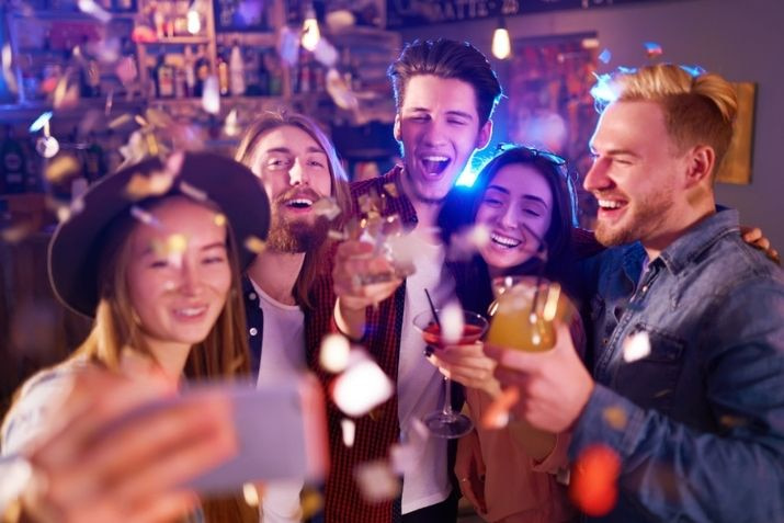 friends laugh and drink and pose for a photo at a bar party