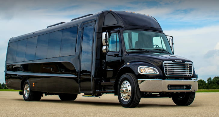 A sleek black party bus parks in front a blue open sky