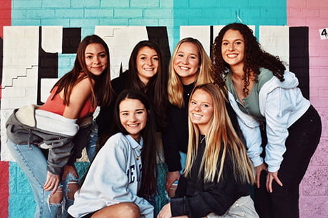 A group of sorority sisters pose for a photo in front of a mural
